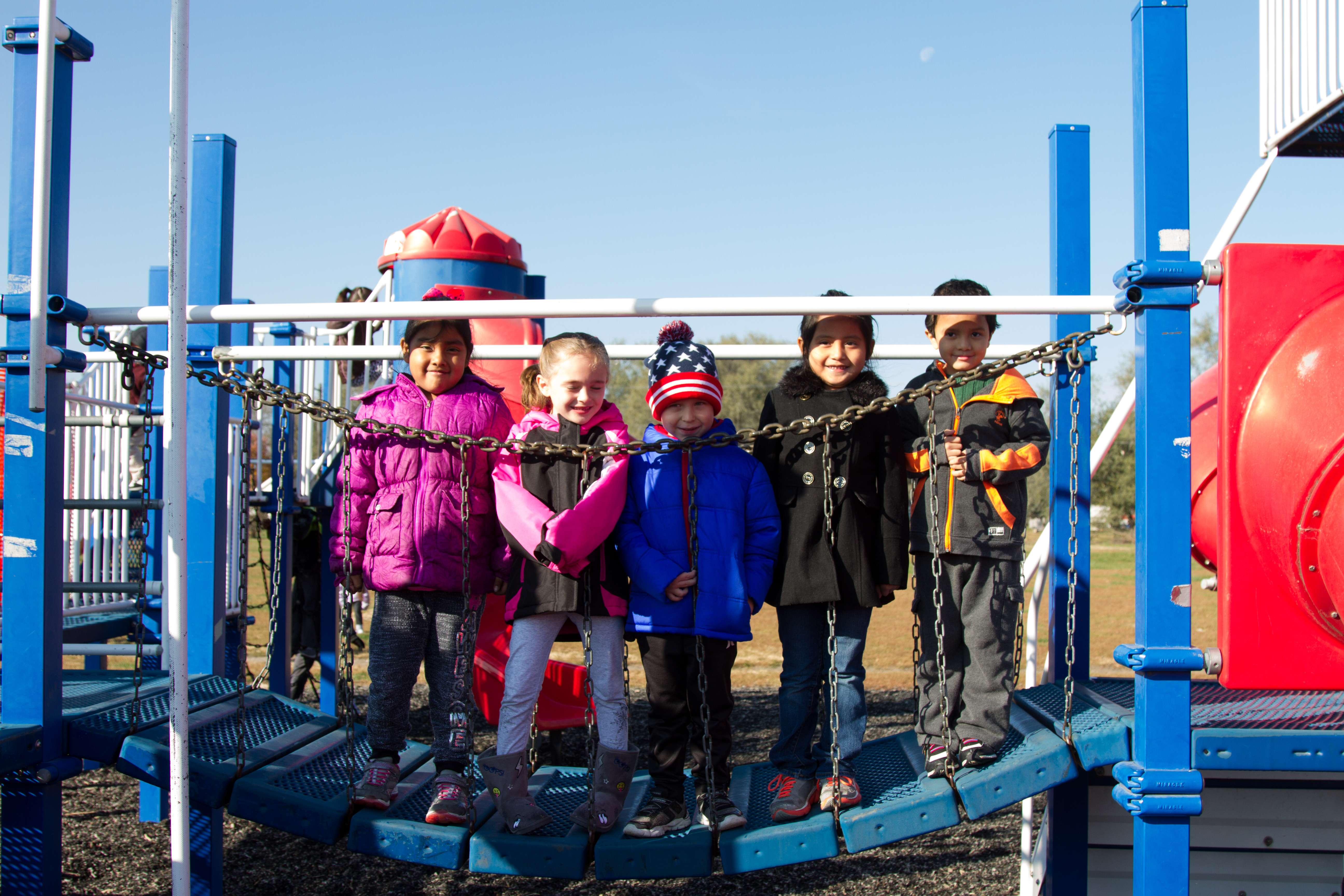 Five young students standing on a hanging bridge at the playground
